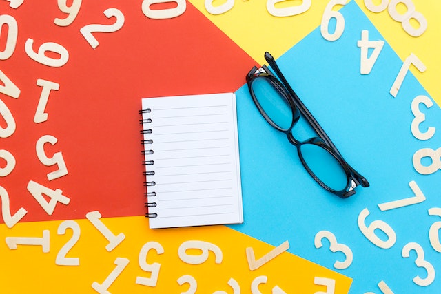 black framed eyeglasses beside notebook with colour papers and counting numbers